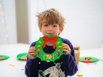 Little boy proudly shows his crafted Christmas wreath