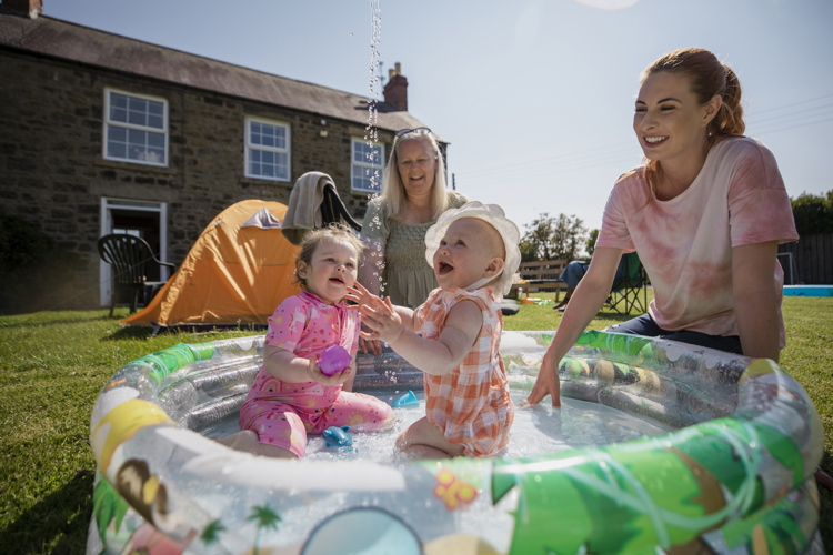 Young children playing in a paddling pool, being supervised by adults
