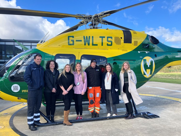 Image of Wiltshire & Bath Air Ambulance helicopter with the Curo team and WBAA colleagues