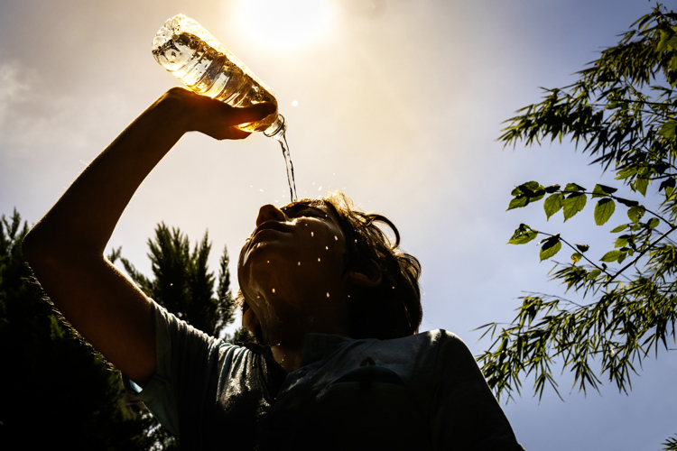 A woman pouring a bottle of water over her head to cool down