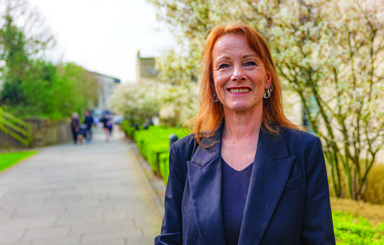 Red haired smiling lady wearing a blazer, stood in one of our community green spaces.