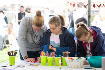 Two children and an adult engage in one of the games at one of the marquee stalls