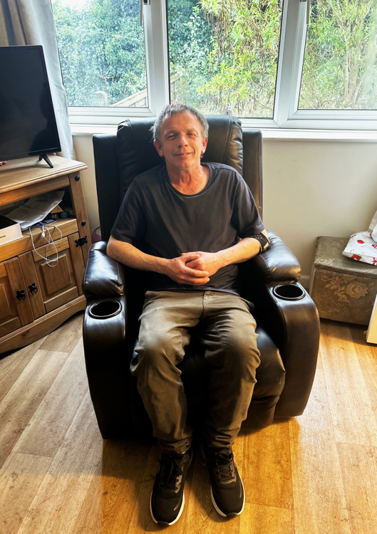 Middle aged man sitting in dark clothes, smiling, in a leather recliner chair