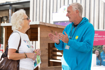 Older lady with white hair and white tshirt, smiling whilst conversing with a Curo Resident Engagement Officer, an older man with grey hair, wearing a blue Curo branded hoody.