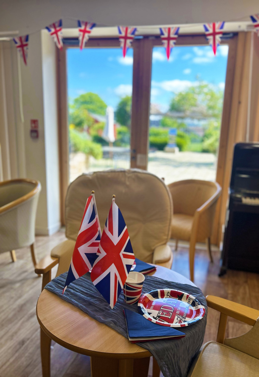 Union Jack flags and bunting hang beautifully in front double doors that have a view of blue, sunny skies and the garden outside.