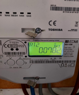 Smart electricity meter with a digital display showing energy consumption in kilowatt-hours (kWh), connected to electrical cables below.