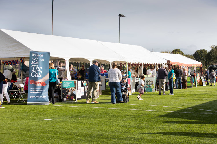 White marquees set up with stalls and colleagues on a grass pitch.