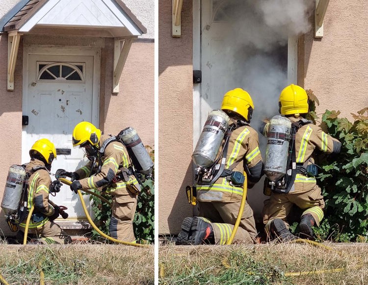 Firefighters in yellow helmets respond to heavy smoke emerging from a house entrance.