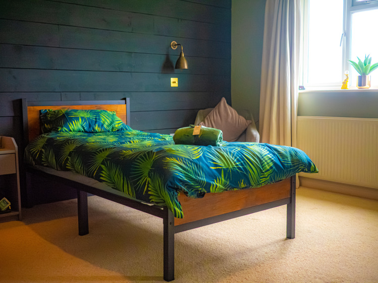 A cosy bedroom with dark teal wooden walls and jungle print bedding on a single bed.