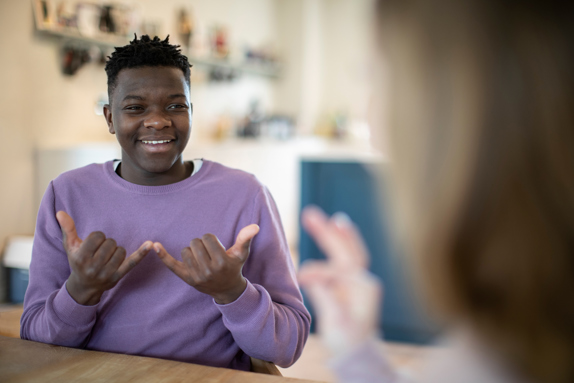 a young black male uses BSL to communicate with another BSL user